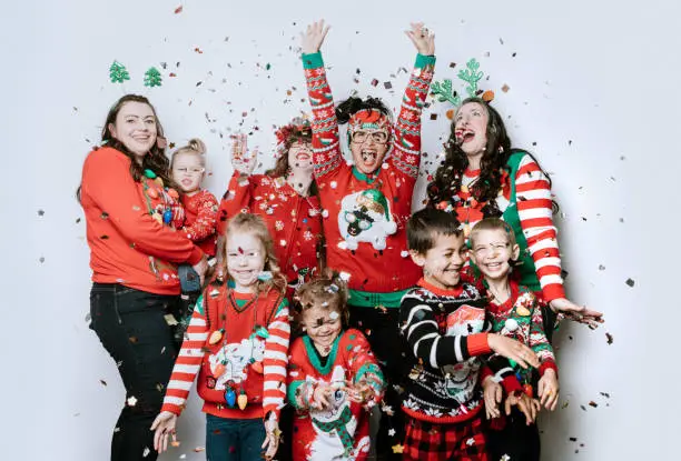 A mothers group and their kids celebrate the holiday taking a portrait wearing "ugly" Christmas sweaters, throwing confetti into the air.