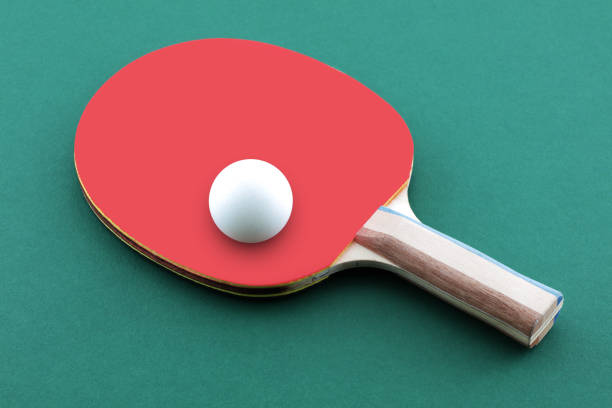 istock Green ping pong table with ball resting on a table tennis bat paddle 1285513740