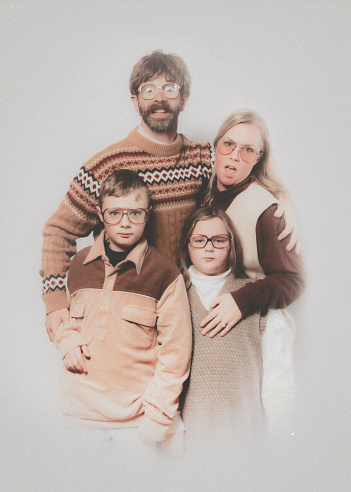 A Caucasian family poses for a portrait in the style of the late 1970's or early 1980's.  They wear matching brown and tan outfits.