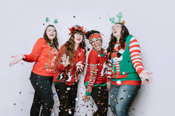 Christmas Ugly Sweater Party With Adult Friends A group of adult women friends celebrate the holiday taking a portrait wearing "ugly" Christmas sweaters, throwing confetti into the air. christmas sweater photos stock pictures, royalty-free photos & images