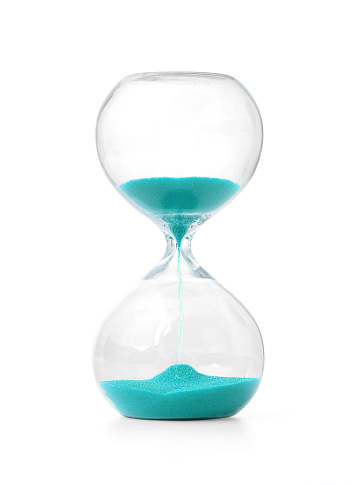 Sand running through the bulbs of an hourglass measuring the passing time in a countdown to a deadline, on a dark floor background with copy space.