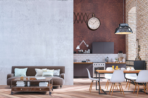 Industrial large modern kitchen with brown wooden kitchen cabinets on white tiled and high rusty wall background. An arched window on orange brick wall and a pendant light over a full dining table with white modern chairs and a retro giant clock on the wall. A living room with a brown sofa and retro table in front of concrete wall background with copy space on hardwood floor. 3d rendered image.