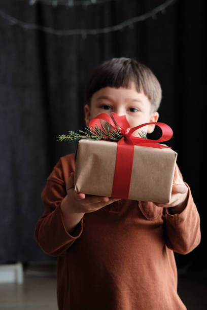 bambino di 4-5 anni in possesso di scatola regalo su sfondo scuro per la festa di natale - surprise child 4 5 years little boys foto e immagini stock