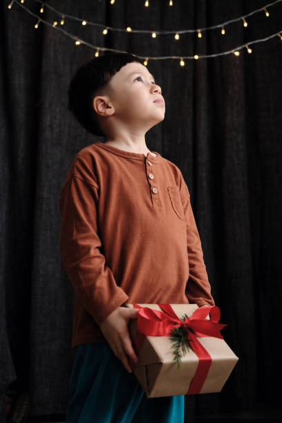 bambino di 4-5 anni in possesso di scatola regalo su sfondo scuro per la festa di natale - surprise child 4 5 years little boys foto e immagini stock