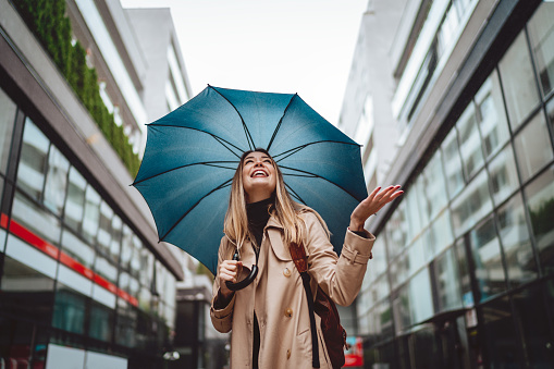 A beautiful smiling young woman walking through the city with an umbrella.