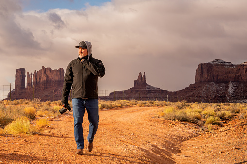 A middle aged Hispanic man walking with a professional camera acting as a photographer or filmmaker in Monument Valley Arizona
