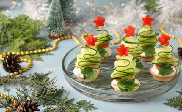 Festive canapes in shape of Christmas trees made of cucumbers and stars of red pepper on light blue background. Horizontal format. Closeup stock photo