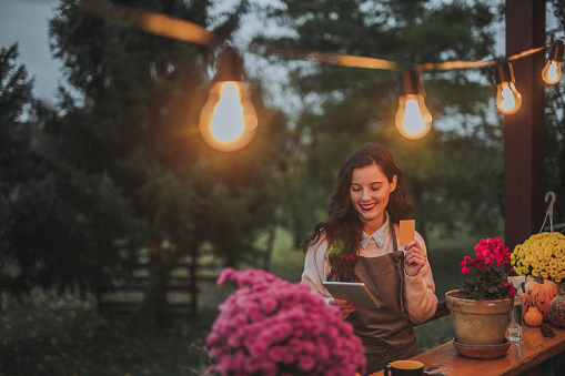 Woman working in flower shop, using digital tablet and holding credit card