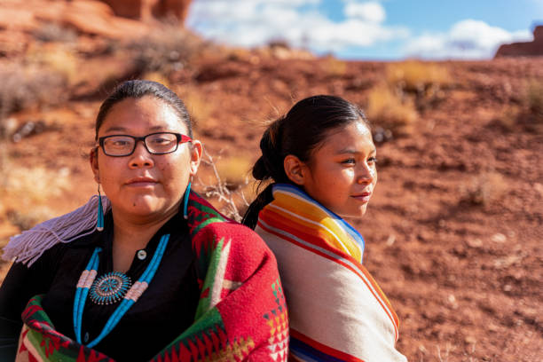전통적인 옷을 입은 나바호 수녀 두 명, 나바호 담요를 뒤로 감싸고, 하나는 기대하고, 다른 한 명은 멀리 바라보고 있습니다. - navajo reservation 뉴스 사진 이미지