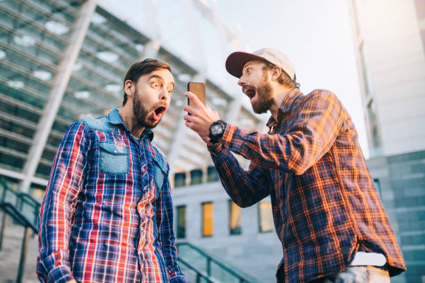 Men being happy winning a bet in online sport gambling application with football stadium on the background Two friends showing sincere emotions of joy about victory in online lottery. Men being happy winning a bet in online sport gambling application with football stadium on the background. jackpot winner stock pictures, royalty-free photos & images