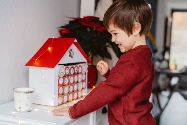 Little happy child opening handmade advent calendar made from toilet paper rolls. Sustainable Christmas, upcycling, zero waste, kids seasonal activities