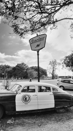 Fredericksburg,Texas - Nov. 12, 2020   Old Antique 1950  Hudson Police Car parked next to 1950's Sinclair Oil Corporation gas sign in black and white.