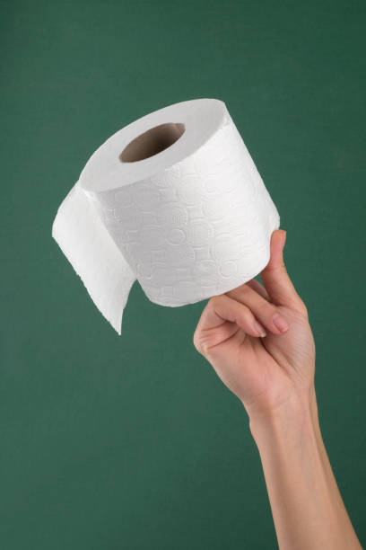 Hand holding white toilet paper roll over green background stock photo