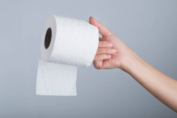 istock Hand holding white toilet paper roll over grey background 1285539236