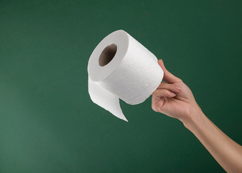 Hand holding white toilet paper roll over green background. Close up shot.