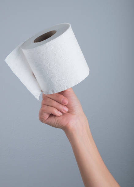 istock Hand holding white toilet paper roll over grey background 1285539305