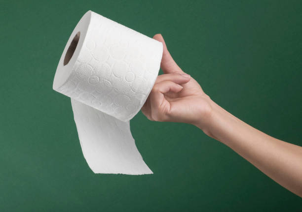 Hand holding white toilet paper roll over green background stock photo