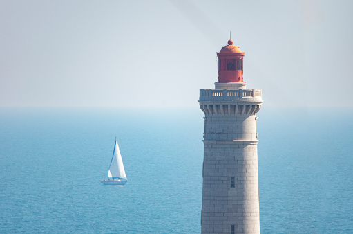Top of a lighthouse on the sea with a sailboat with a clear sky