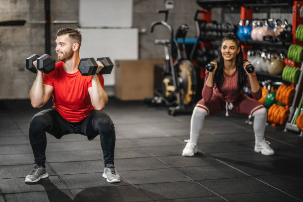 jóvenes atléticos haciendo sentadillas con pesas, los deportistas jóvenes están haciendo ejercicio con mancuernas y sonriendo en el gimnasio - stretching boyfriend indoors lifestyles fotografías e imágenes de stock