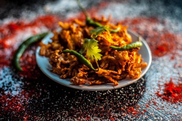 tiré de piyaz pakora/bhaji/bhajji/bhajiya/bajji dans une plaque de verre avec quelques piments verts frais et de la poudre de chili rouge avec elle sur la surface noire. - shot glass glass black empty photos et images de collection