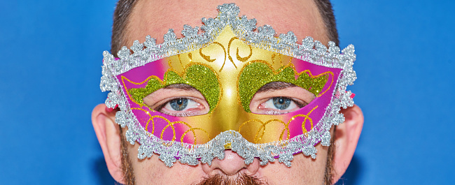 Closeup portrait of man in Mardi gras masquerade mask in complementary art. Funny face during celebration Mardi Gras, banner copy space