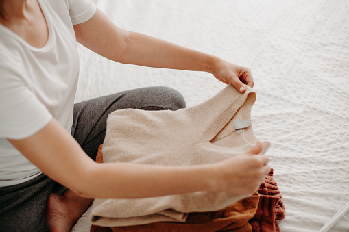 Mujer organizando ropa de abrigo de otoño e invierno. Joven doblando suéteres en cama blanca. Lavandería plegable. photo