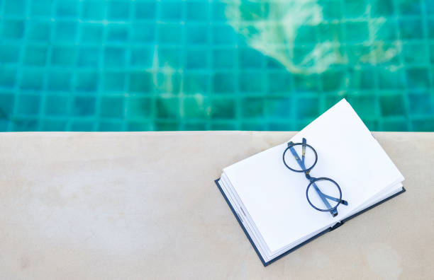 istock Eyeglasses on blank notebook on swimming pool edge with space on blurred blue water background 1285577988