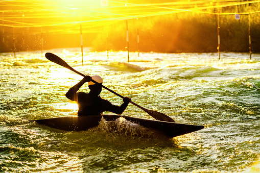 Sillouette of kayaker rowing against the stream at sunrise