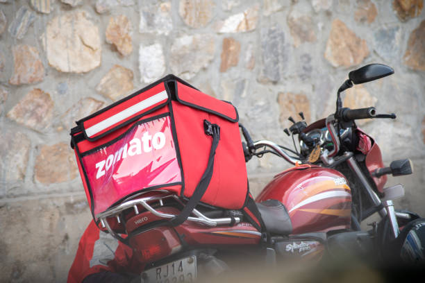 Bike with a large red zomato food delivery bag belonging to a rider of the food delivery unicorn startup in India Delhi, India - circa 2020 : Bike with a large red zomato food delivery bag belonging to a rider of the food delivery unicorn startup in India which has gained huge popularity during the COVID pandemic with people ordering out and eating from home with riders taking high risk and low paid jobs ZOMATO stock pictures, royalty-free photos & images