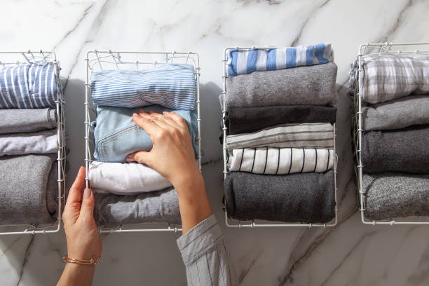 Neatly folded clothes and pyjamas in the metal mesh organizer basket on white marble table