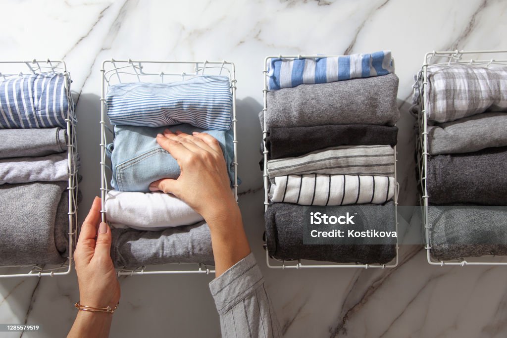 Neatly folded clothes and pyjamas in the metal mesh organizer basket on white marble table Neatly folded clothes and pyjamas in the metal mesh organizer basket on white marble table. modern style of garments declutter and sorting concept. Housewife using modern method of tidying up. Organization Stock Photo
