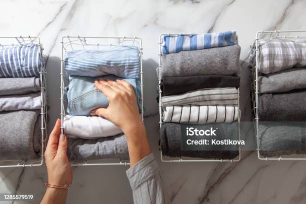 Neatly Folded Clothes And Pyjamas In The Metal Mesh Organizer Basket On White Marble Table Stock Photo - Download Image Now