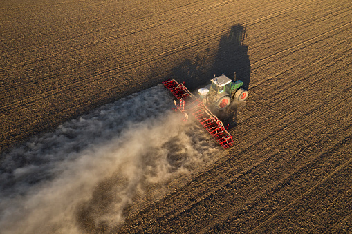 Aerial view of a farm tractor with seed drill sowing plowed field in springtime.