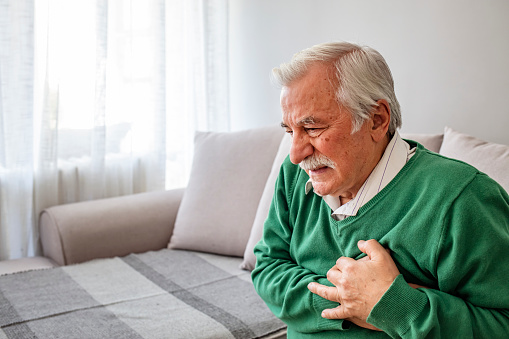 Senior man suffering from heart attack at home. Man clutching his chest. Pain, possible heart attack. Senior adult. Senior having heart attack at home. Old man holding breast because of heart infarction