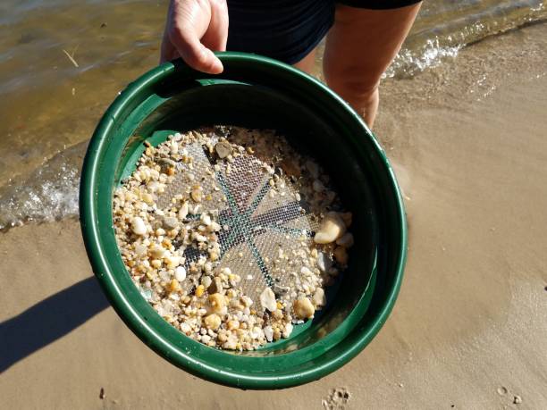 istock female hand holding strainer with stones at beach with water 1285598247