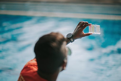 Asian indian lifeguard Pool testing kit being used in a swimming pool for water chlorine level