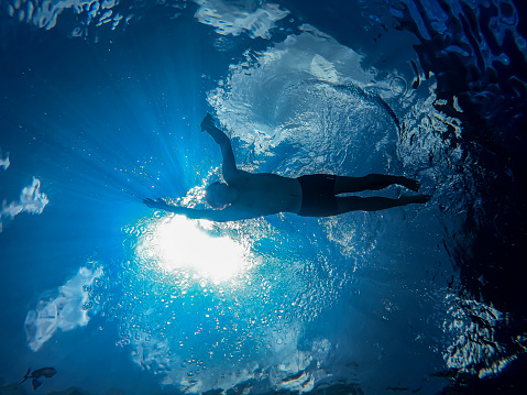 Above top view portrait of young adult caucasian female model in sport black swimsuit stand in clear blue water of indoor swimming pool at dark evening time. Relax harmony and wellness spa therapy.