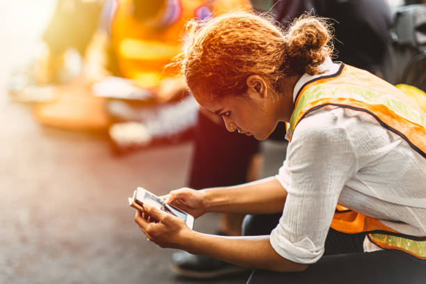 Black African American woman break relaxes and reads the news on her mobile smart phone in an industrial factory. Black African American woman break relaxes and reads the news on her mobile smart phone in an industrial factory. construction lunch break stock pictures, royalty-free photos & images