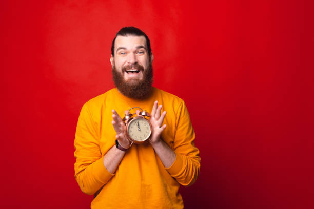 istock Cheerful bearded man is holding a clock with both hands looking at the camera 1285607365