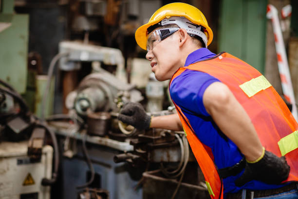 i lavoratori asiatici che lavorano sodo nelle fabbriche industriali soffrono di mal di schiena mentre lavorano sulle macchine. - physical injury backache occupation working foto e immagini stock