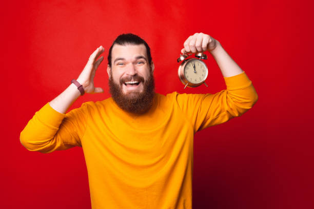 istock A bearded man is holding a clock looking at the camera is smiling 1285607717
