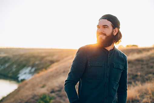 Portrait of smiling bearded hipster man outdoor at sunset, happy traveler.