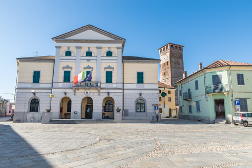 San Nazzaro Sesia, Italy - October 12, 2020: Typical Italian square with stone paving, the town hall and the 11th century romanesque bell tower of the abbey of Santi Nazario e Celso. Piedmont region. Small town in the province of Novara, in the Po valley