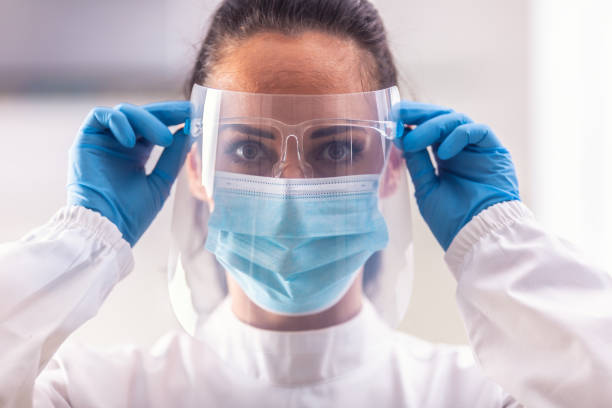 istock Female medic puts on protective shield and other equipment not get infected by coronavirus. 1285615980