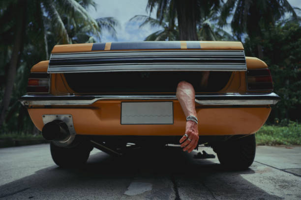 dead body hand protrudes from the trunk of a yellow classic car stock photo