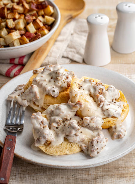 Biscuits and Sausage Gravy Biscuits and creamy sausage gravy on a plate with fried potatoes in background gravy stock pictures, royalty-free photos & images