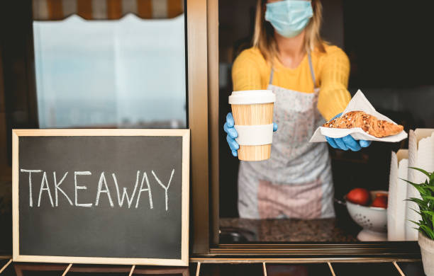 istock Young woman wearing face mask while serving takeaway breakfast and coffee inside bakery cafeteria - Worker preparing healthy organic food inside cafe' kitchen during coronavirus outbreak 1285624832