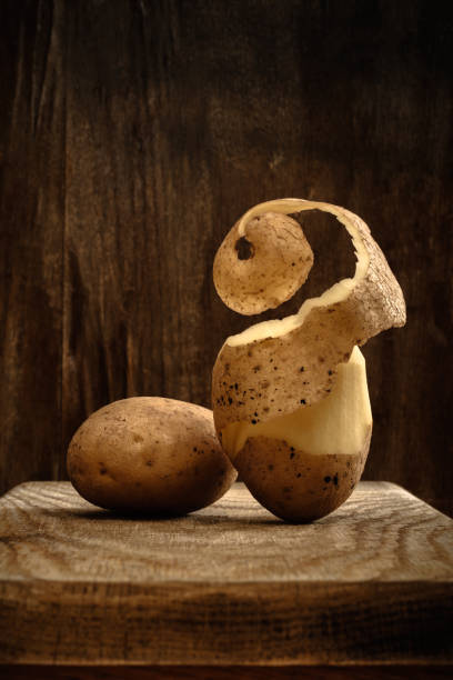 un paio di patate crude fresche con una buccia verso l'alto tagliata verso l'alto su una tavola su un vecchio sfondo di legno. vista laterale. concetto di cibo minimalista rustico artistico in toni marroni con spazio di copia per layout creativo - vista verso lalto foto e immagini stock