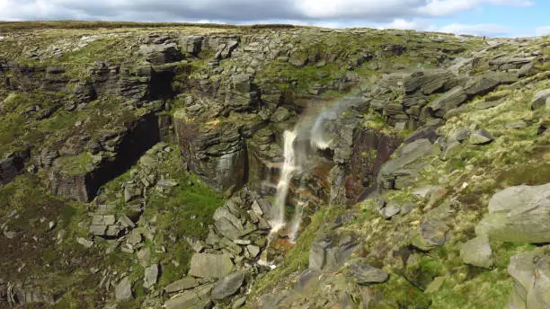 Kinder Downfall in Peak District National Park. Probably the biggest waterfall in Peak District. Falling off Kinder Scout plateau. Becouse strong opposite wind part of water is flying up, back. Besides there is a rainbow on this downfall visible.