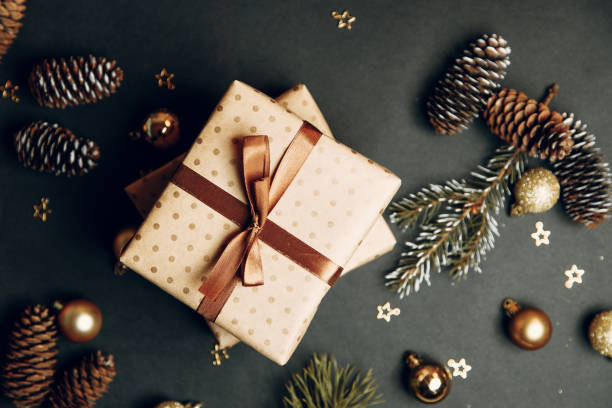 istock Christmas composition with a gift in a box. Golden toys, modern holiday decorations, gift boxes, fir branches on a dark black background. Elegant Christmas greeting card template. 1285636748